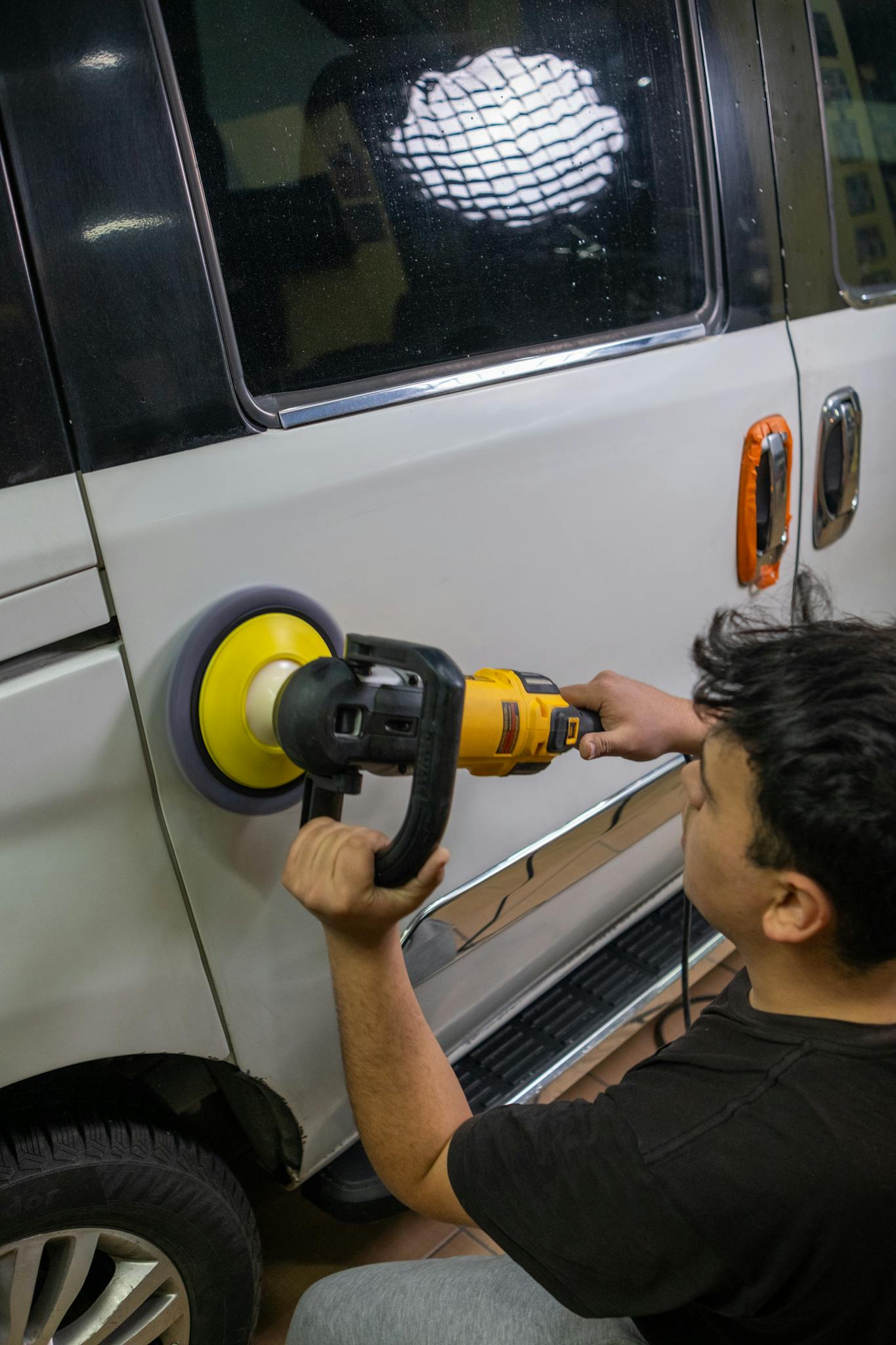 A person polishing a car with a buffer in an automotive repair workshop.