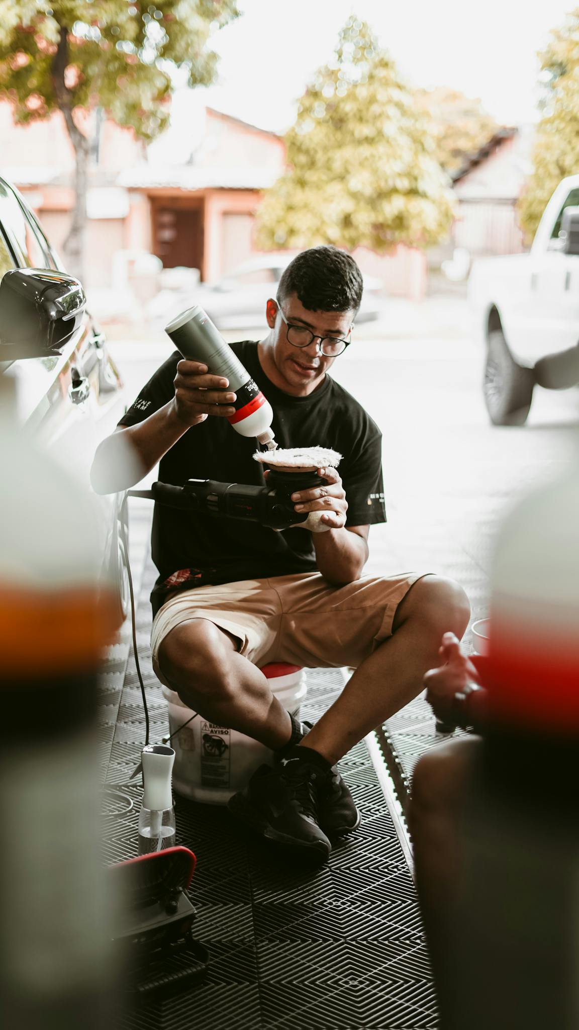 Young man using a rotary polisher on a car, outdoors, creating a vibrant shine.